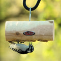 Downy woodpecker feeding from a hanging cedar log suet feeder for backyard birds.