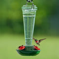 8 oz. Torchiere Glass Hummingbird Feeder with red flower ports and embossed green glass, attracting a hummingbird as it hovers to drink nectar.