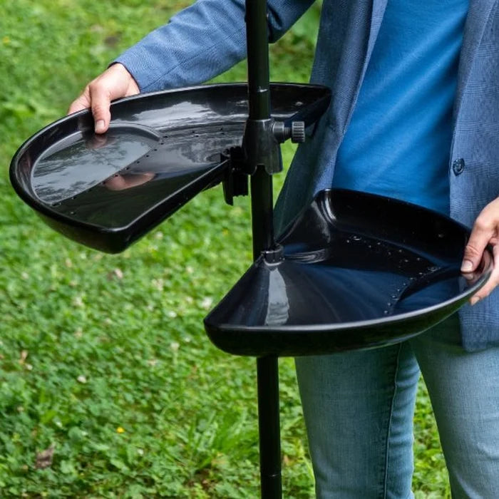 Person adjusting Brome Seed Buster Seed Tray and Catcher, featuring two adjustable black trays on a pole, designed to reduce bird seed waste and facilitate cleaning.