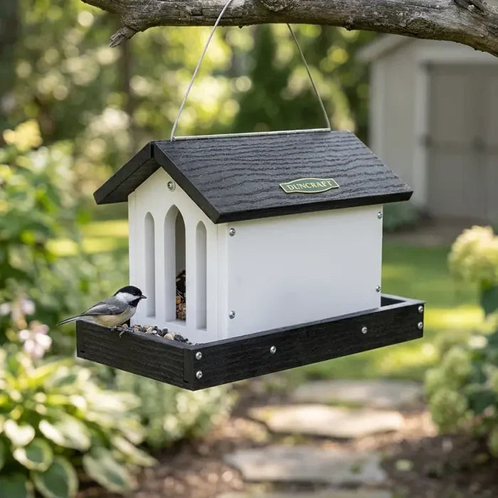 Bird feeder hanging from a tree branch with a bird perched on it, set against a natural outdoor background.