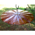 Extra Large Hanging Disk Squirrel Baffle, Copper Tint, shown outdoors; a circular, metal baffle designed to deter squirrels, hanging from a pole.