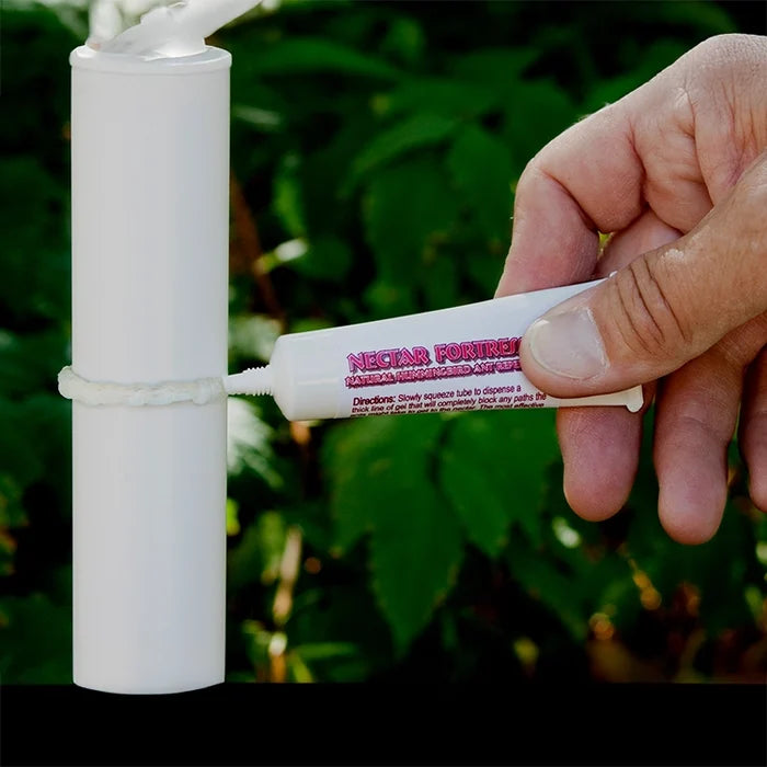 Hand applying Nectar Fortress Natural Hummingbird Ant Repellent gel on a PVC pole, forming a barrier to effectively repel ants from nectar feeders.