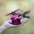 Hand holding Perky-Pet Handheld & Tabletop Hummingbird Feeder with three flower ports, ideal for feeding and watching hummingbirds closely.