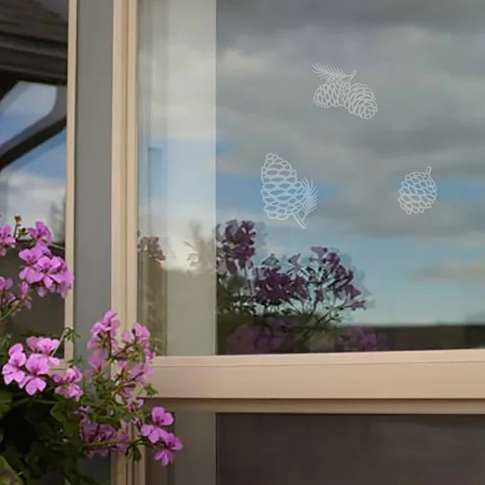 Window with decorative pine cone decals and purple flowers in the foreground