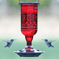 Red Jewel Hummingbird Feeder with embossed decorative hummingbirds, red flower-shaped feeding ports, metal hanger, and wraparound perch, attracting two flying hummingbirds.